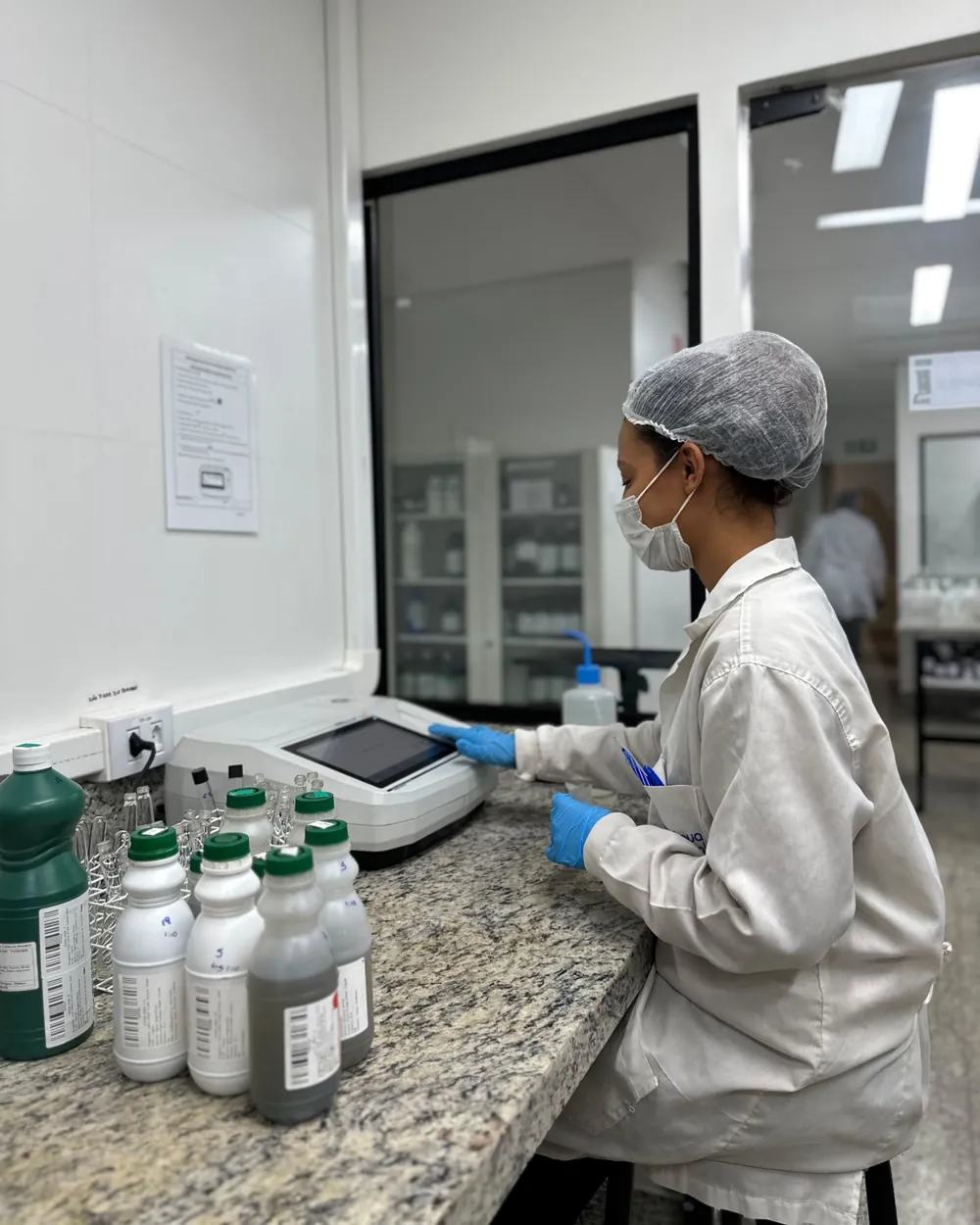 Analista da Conágua Ambiental operando um espectrofotômetro ao lado de frascos de amostras identificados por código de barras