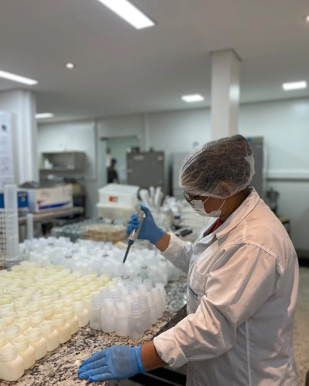 Analista da Conágua Ambiental pipetando amostras em frascos de coleta no laboratório